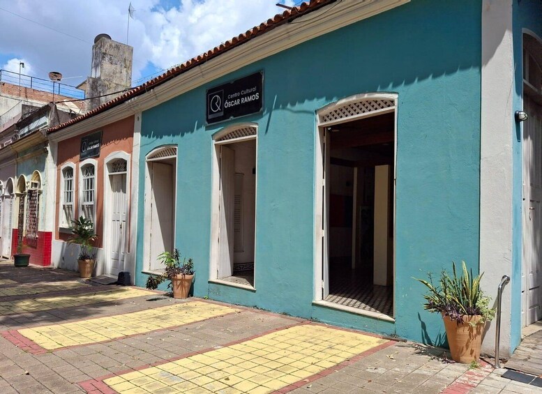 A street with buildings painted in various colors, a sign for 'Centro Cultural Óscar Ramos,' and potted plants. 5