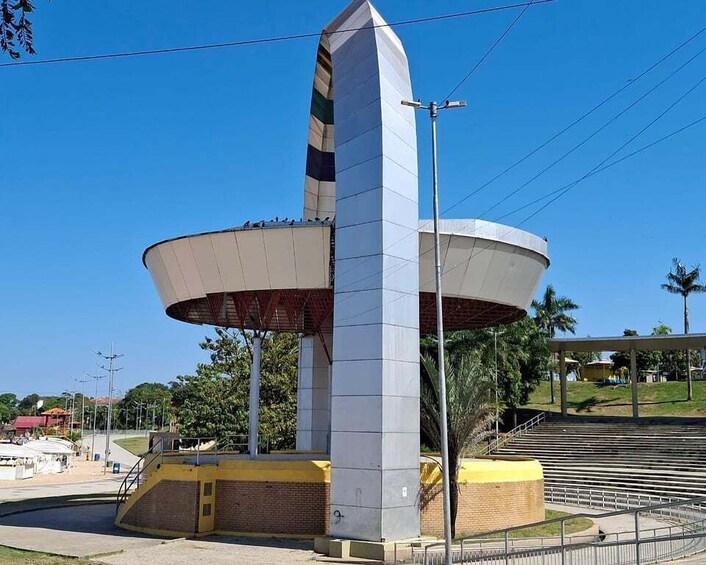 A large, white, multi-tiered monument with a pointed top, surrounded by a brick base and a yellow border, set against a clear blue sky. 4