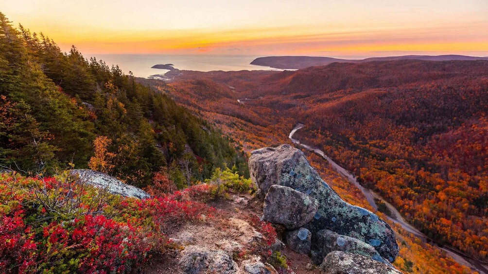 A mountainous landscape with autumn foliage, a winding road, and a body of water in the distance. 3