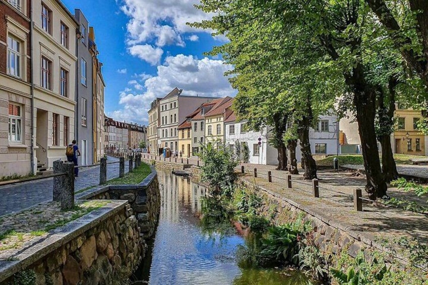 A canal with buildings on either side, a stone bridge, and a tree-lined path. 5