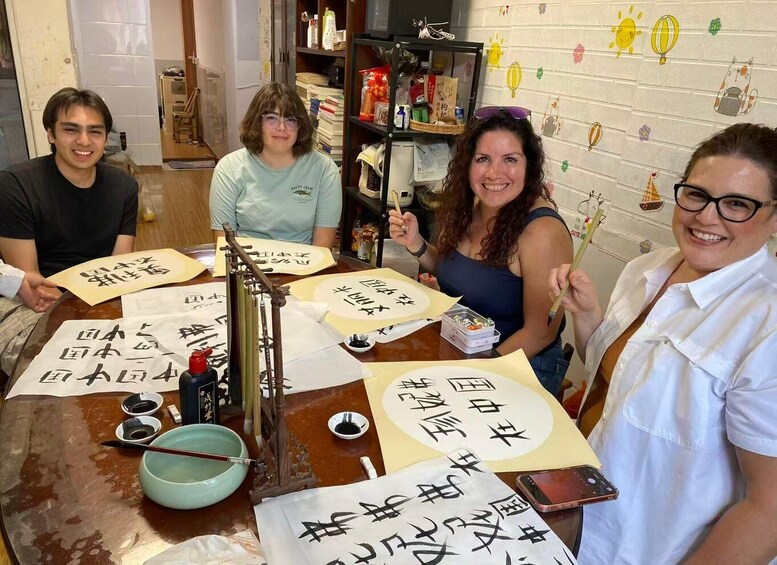 Four people engaged in calligraphy, with ink bowls, brushes, and paper on a table. 1