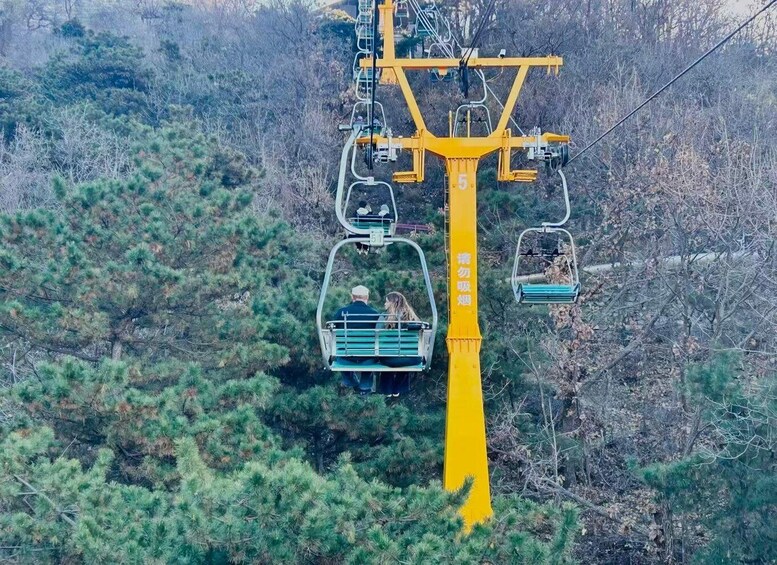 A cable car system with two cabins suspended from a yellow structure amidst a forested area. 5