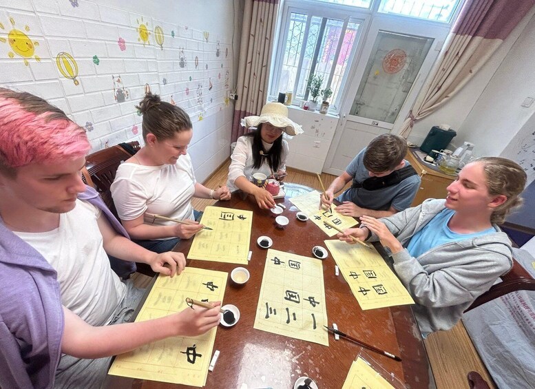 A group of people engaged in calligraphy practice, with paper sheets and brushes on a table. 3
