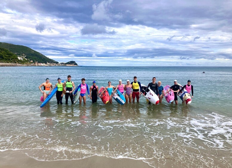 A group of people standing in shallow water on a beach, holding surfboards. 3