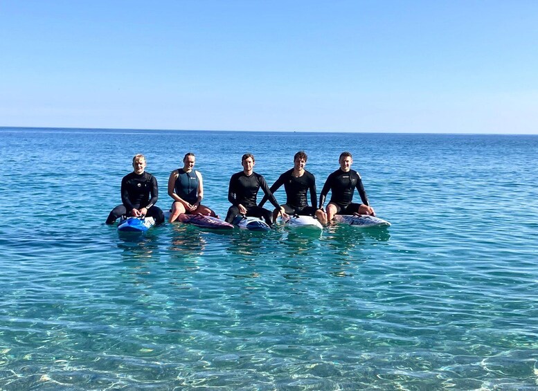 Five people sitting on surfboards in clear blue water. 4
