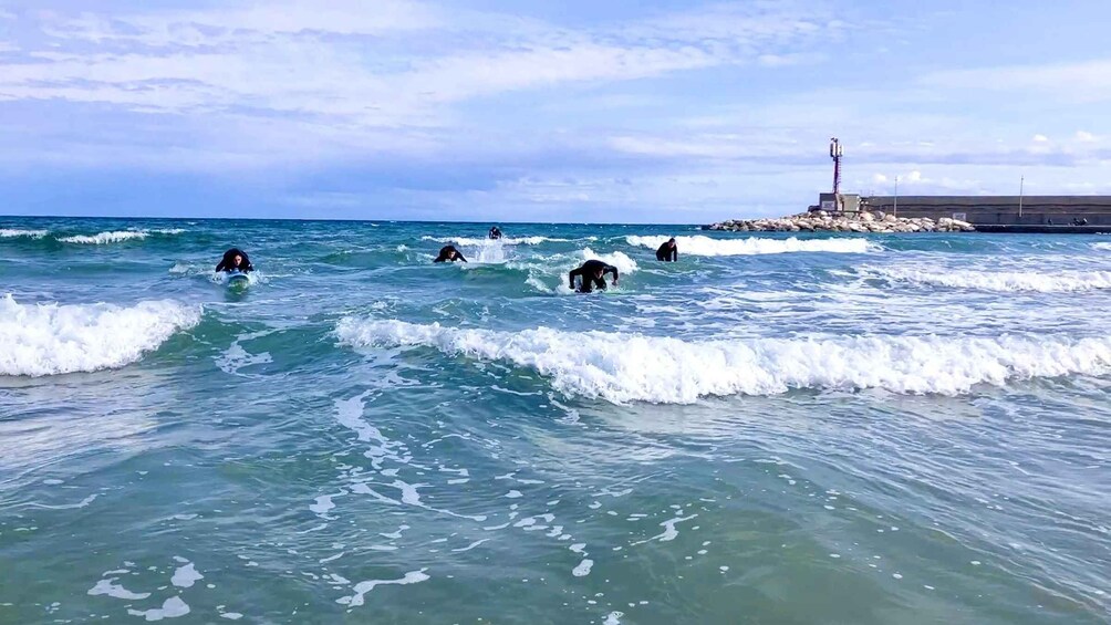Surfers in the ocean with waves, a rocky outcrop, and a lighthouse in the background. 5