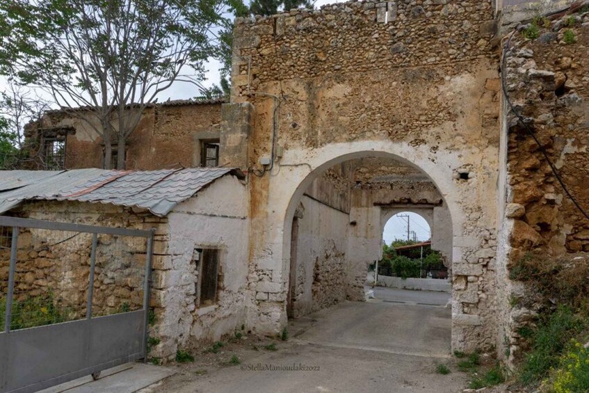 An old stone archway leading into a narrow alley with a rustic building on one side. 5