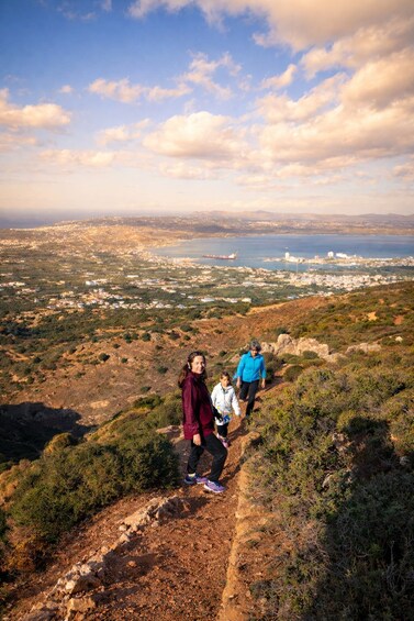 A group of people hiking on a rocky trail with a coastal cityscape in the background. 5