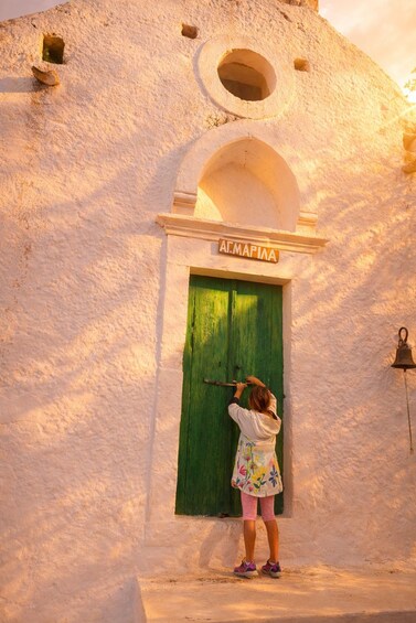 A child ringing a bell at a white building with a green door and a sign reading 'Al-Mapina'. 2