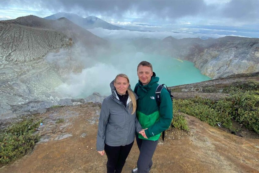 Two people standing on a rocky path with a lake and mountains in the background. 3