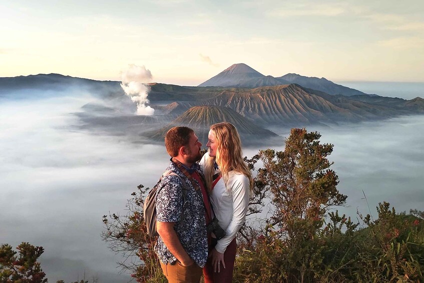 A couple standing on a hill overlooking a volcanic landscape with a mountain in the background. 2