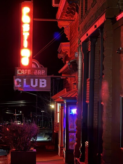 A neon-lit sign for a cafe bar and club, with a brick building and a small garden in the foreground. 5