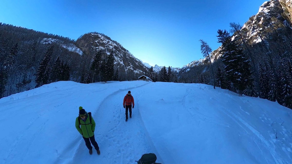 Two people hiking on a snow-covered trail with a mountain and trees in the background. 2