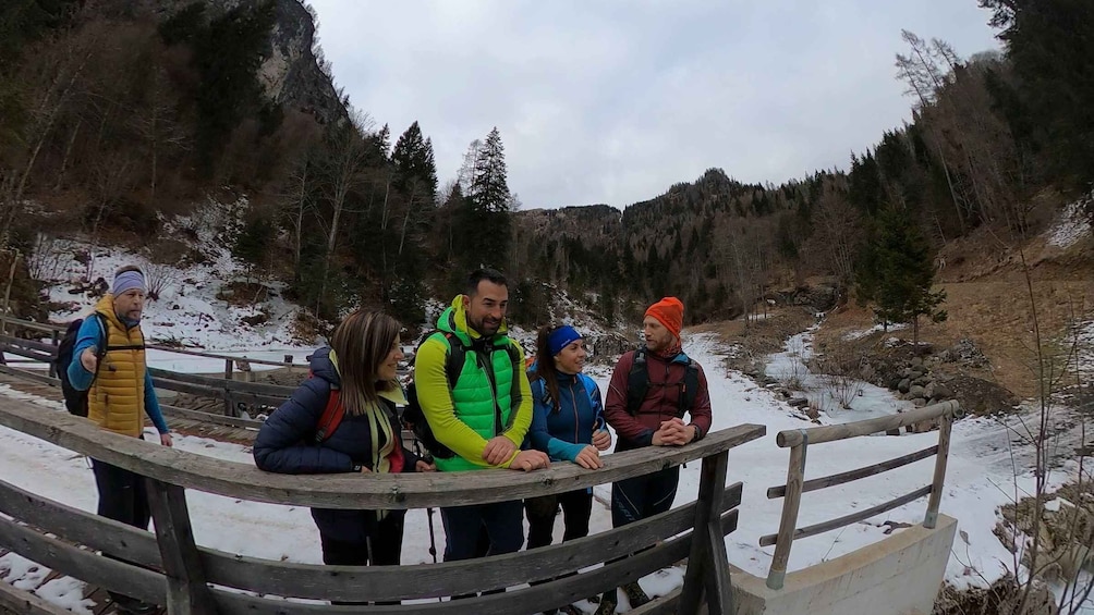 A group of people standing on a wooden bridge over a river, surrounded by trees and snow. 4
