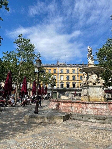 A public square with a fountain, red umbrellas, and historic buildings. 3