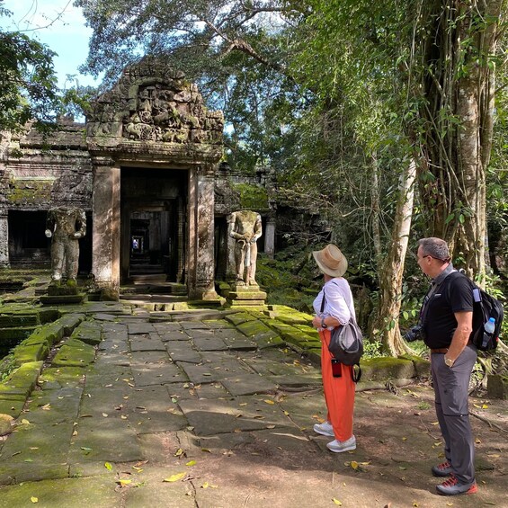 A stone temple entrance with intricate carvings, a person taking a photo, and a guide standing nearby. 2