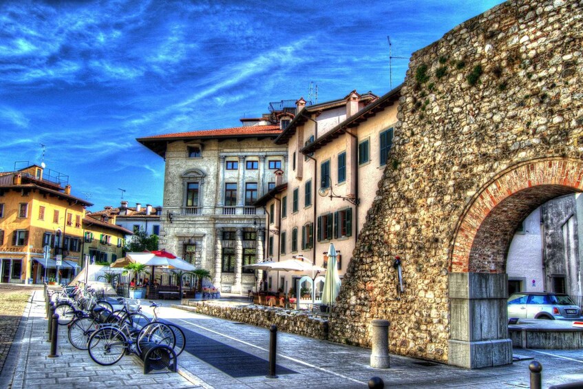 A cobblestone street with historic buildings, a stone archway, and bicycles parked along the sidewalk. 5