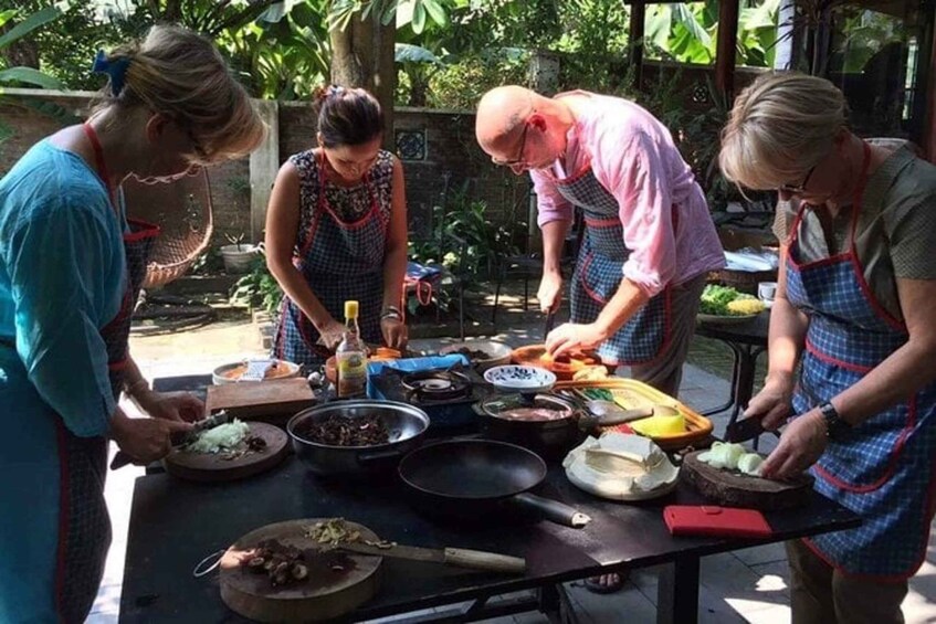 A group of people preparing food outdoors with various cooking utensils and ingredients on a table. 4