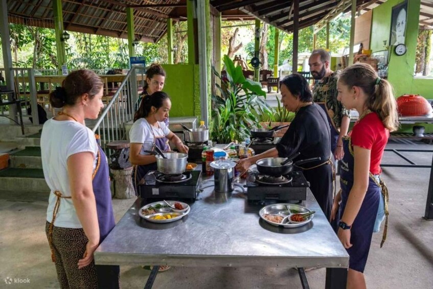 A group of people cooking outdoors with a metal table, pots, and plates of food. 2