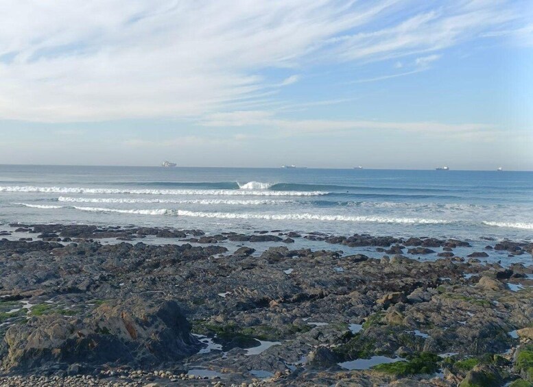 A rocky shoreline with waves, a clear sky, and distant ships. 5