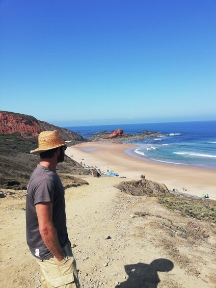 A man in a hat overlooking a beach with red cliffs and a clear blue sky. 5
