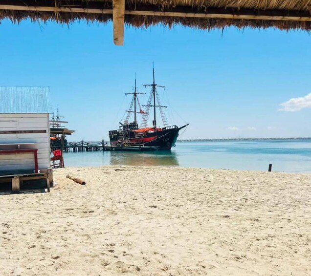 A beach with a wooden pier and a sailing ship anchored near the shore. 1