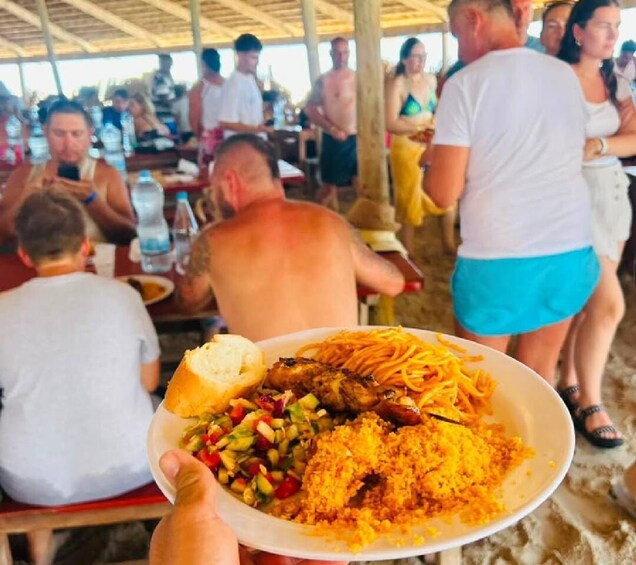 A person holding a plate with food, a crowded outdoor dining area, and people sitting at tables. 4