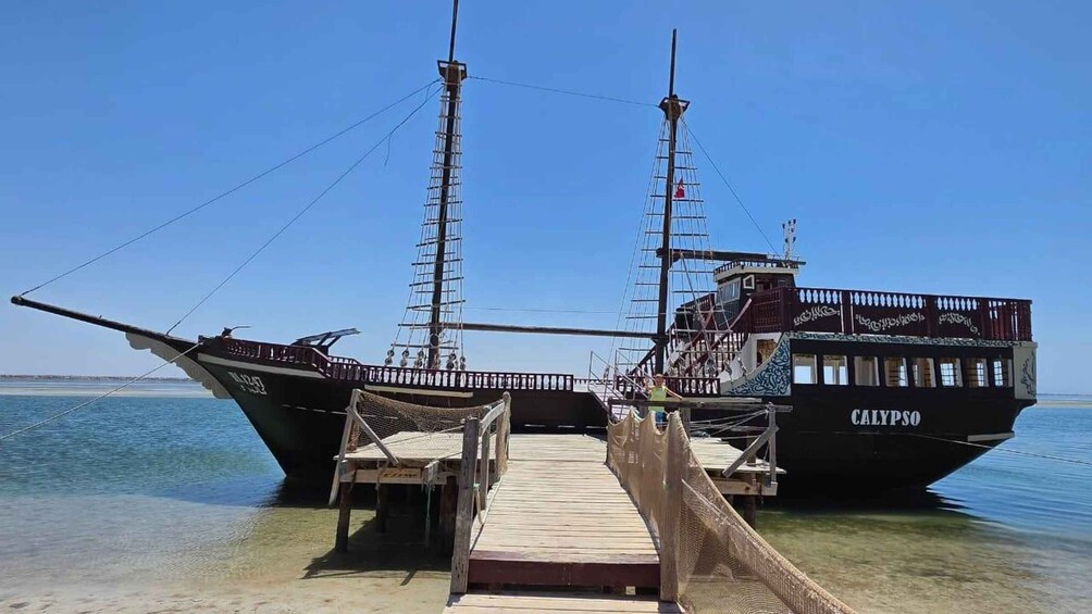 A sailing ship named CALYPSO docked at a wooden pier. 5