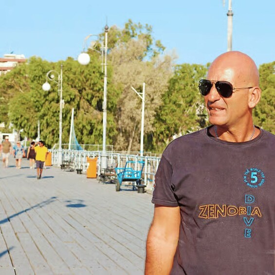 A man walking on a wooden boardwalk with benches and street lamps. 3