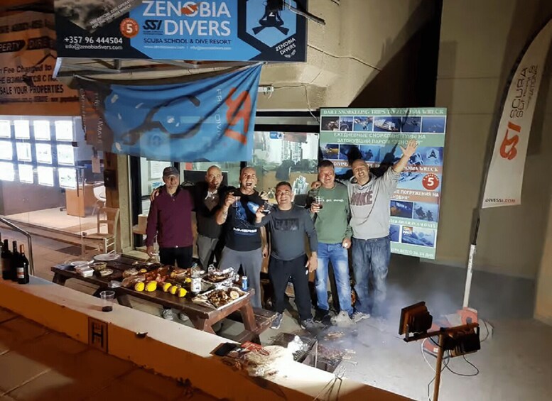 A group of people at a booth with a blue banner, a table with food and drinks, and a smoke machine. 4