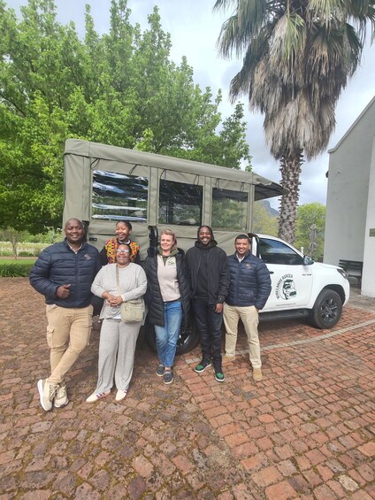 A group of people standing in front of a safari vehicle and a palm tree. 4