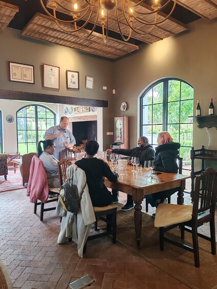 A group of people seated around a wooden table in a room with a rustic ceiling and large windows. 2