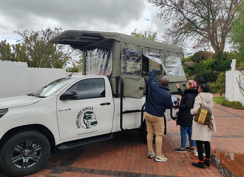 A white pickup truck with a canopy, parked on a brick path with people around it. 1