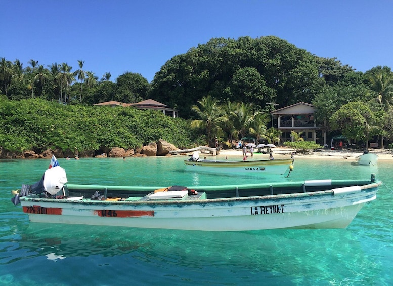 A boat named 'SARA 4' anchored near a beach with palm trees and houses in the background. 2