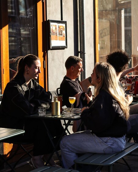 People sitting at an outdoor cafe with drinks and a menu board. 1