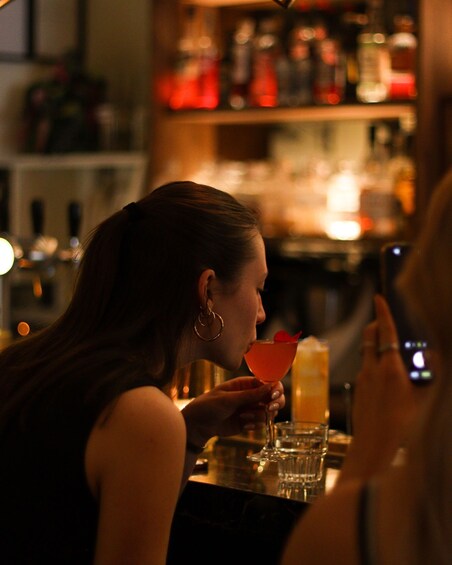 A person holding a cocktail glass at a bar with bottles in the background. 3