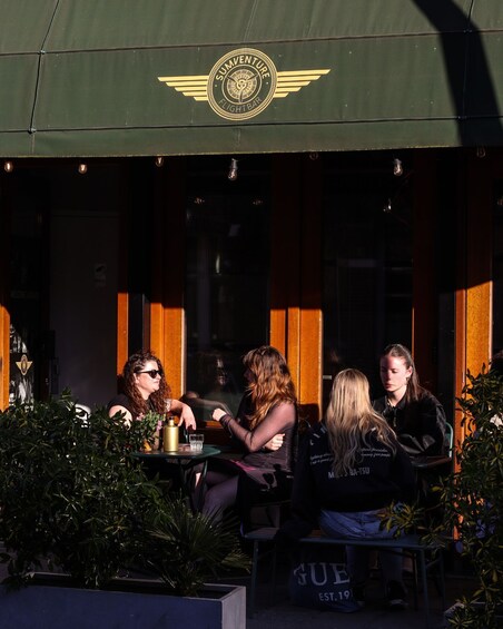 A group of people seated at an outdoor cafe with a green awning displaying a logo. 5