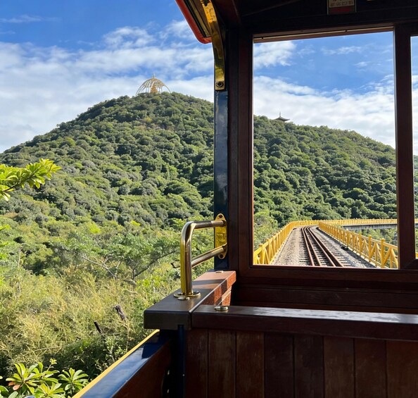 A train window overlooking a lush green mountain with a pagoda-like structure. 5