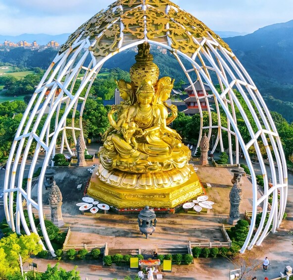 A golden Buddha statue within a white dome structure, surrounded by a garden and a mountainous backdrop. 1