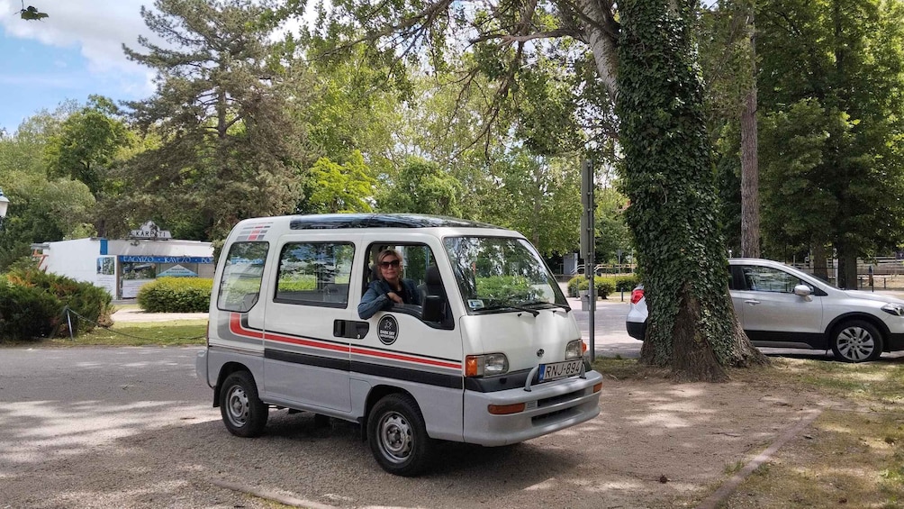 A white van parked on a street with trees and a building in the background. 3