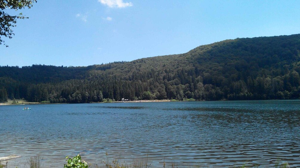 A calm lake with a small boat, surrounded by dense forest and hills. 4