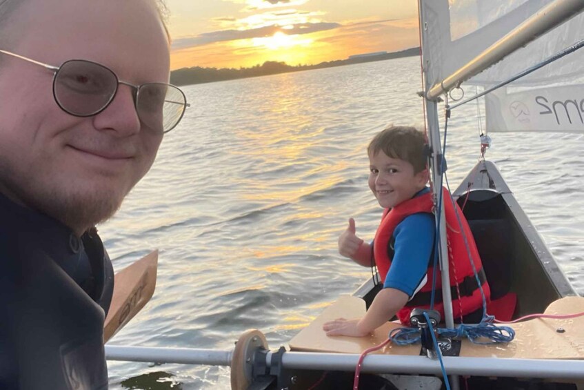 A person on a sailboat with a child wearing a life jacket, water in the background, and a sunset. 2