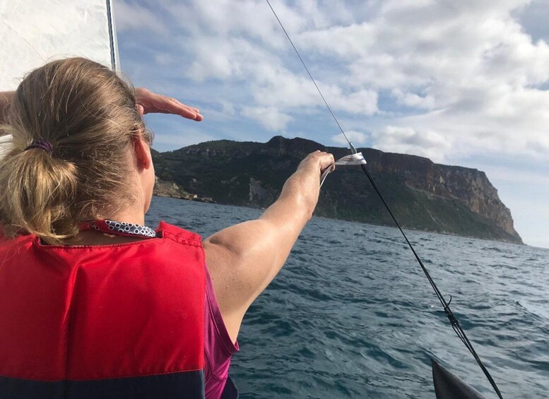 A person on a sailboat, holding a fishing line, with a mountainous coastline in the background. 4