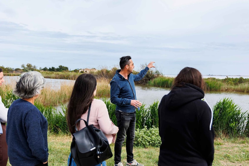 A group of people standing by a body of water, with one person gesturing towards the water. 5