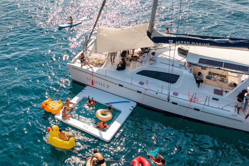 A yacht named 'SUMMER' with people on deck and inflatable toys in the water. 1