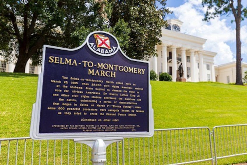 A historical marker sign in front of a white building with columns. 4