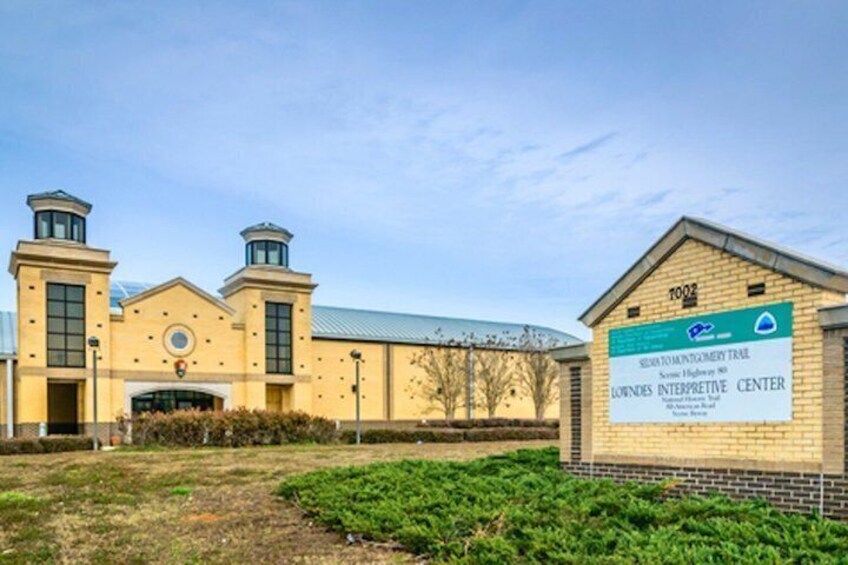 A building with a sign for the Lowndes Interpretive Center, a brick structure with two towers, and a green field in front. 4