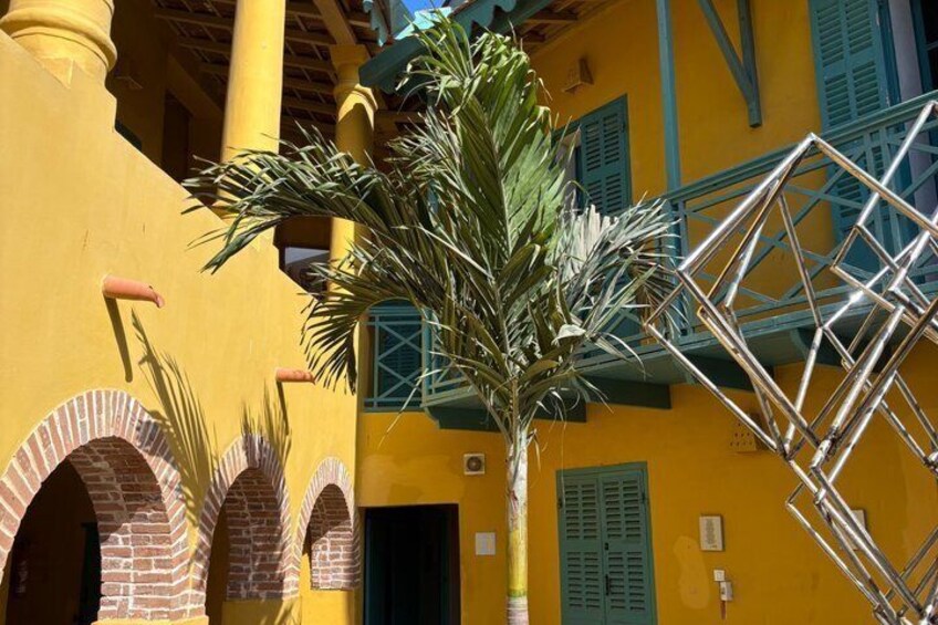 A yellow building with blue shutters, a palm tree, and a metal staircase. 5
