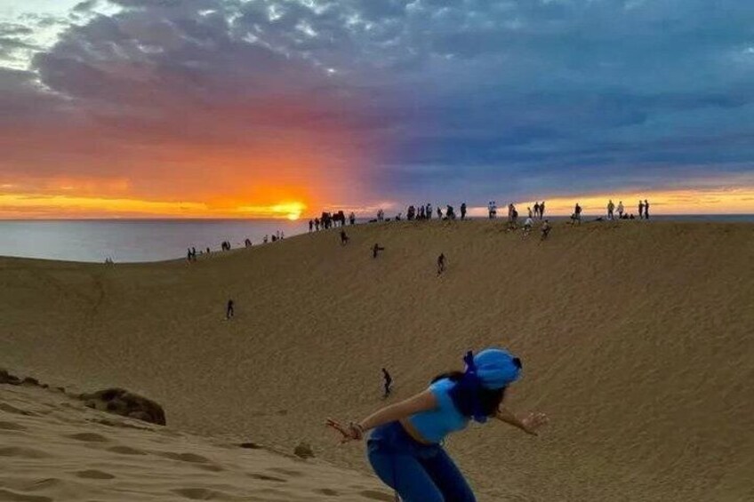 A desert landscape with a sunset, sand dunes, and people walking. 1