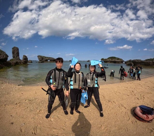 A group of people in wetsuits on a sandy beach with rocky formations in the background. 4